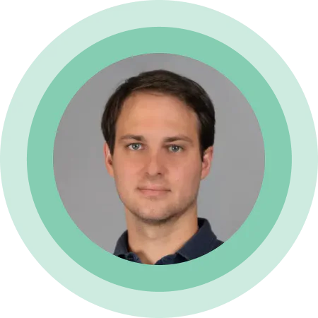 A headshot of a man with a neutral expression and a mint green circular border around the image.