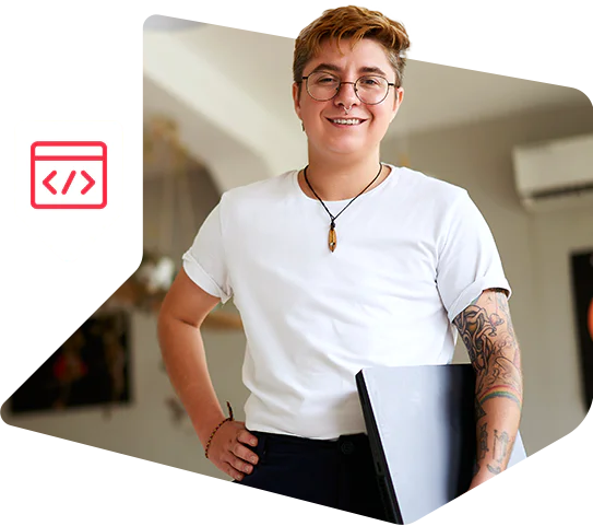 Person with glasses and tattoos holding a laptop, standing indoors Person with glasses and tattoos holding a laptop, standing indoors