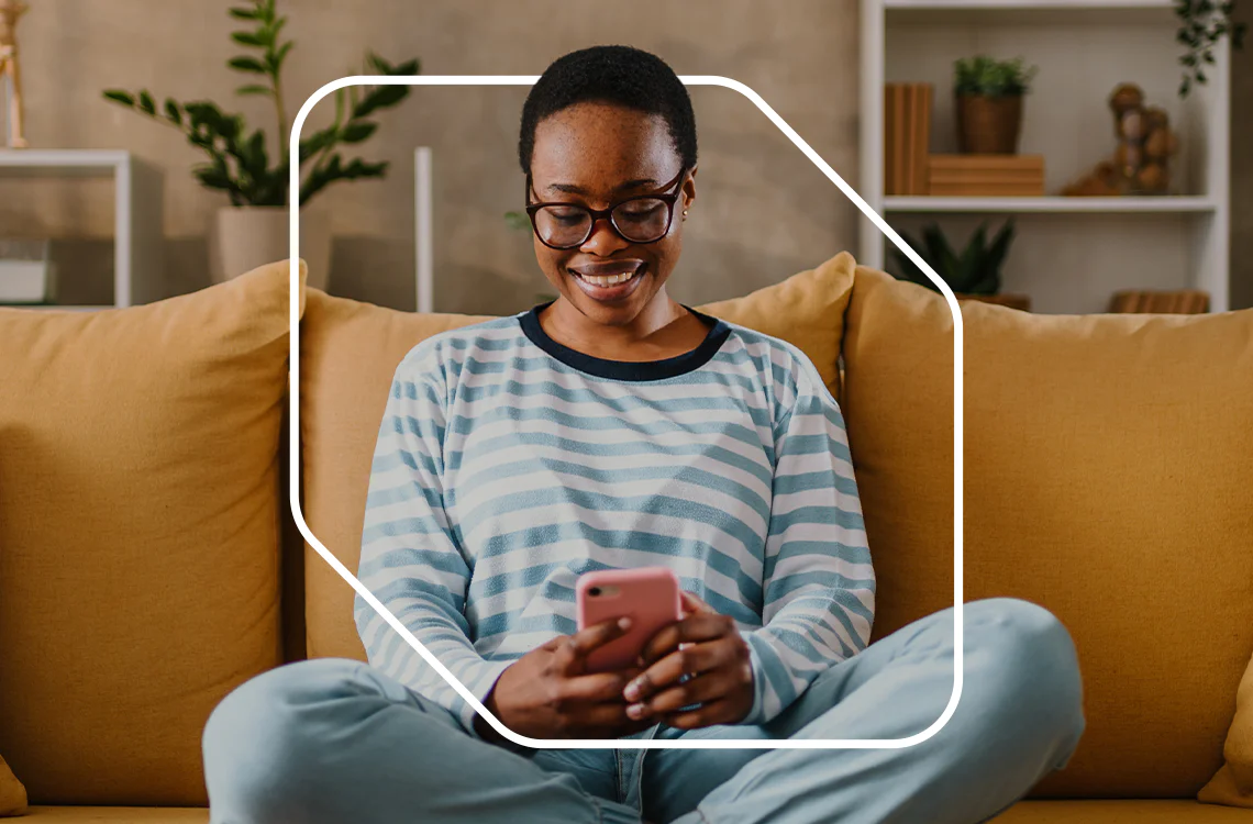 Person in striped shirt smiling at phone on a yellow couch Person in striped shirt smiling at phone on a yellow couch