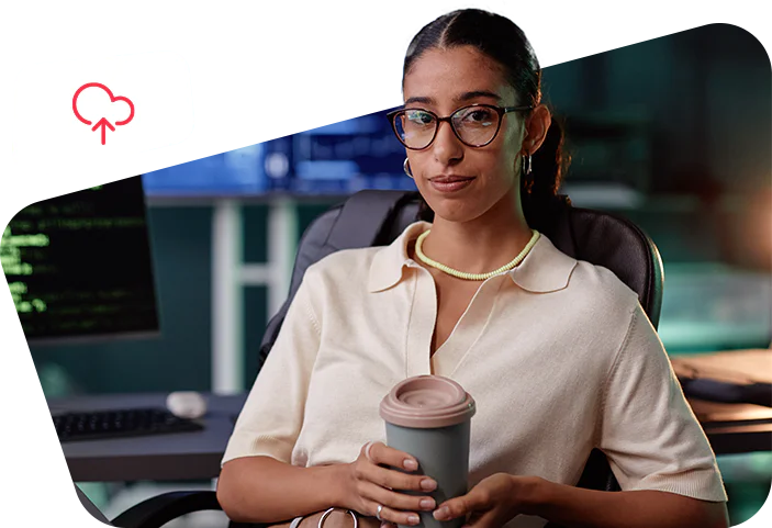 Woman wearing glasses, holding a coffee cup, sitting in front of a computer showing a cloud upload icon. Woman wearing glasses, holding a coffee cup, sitting in front of a computer showing a cloud upload icon.